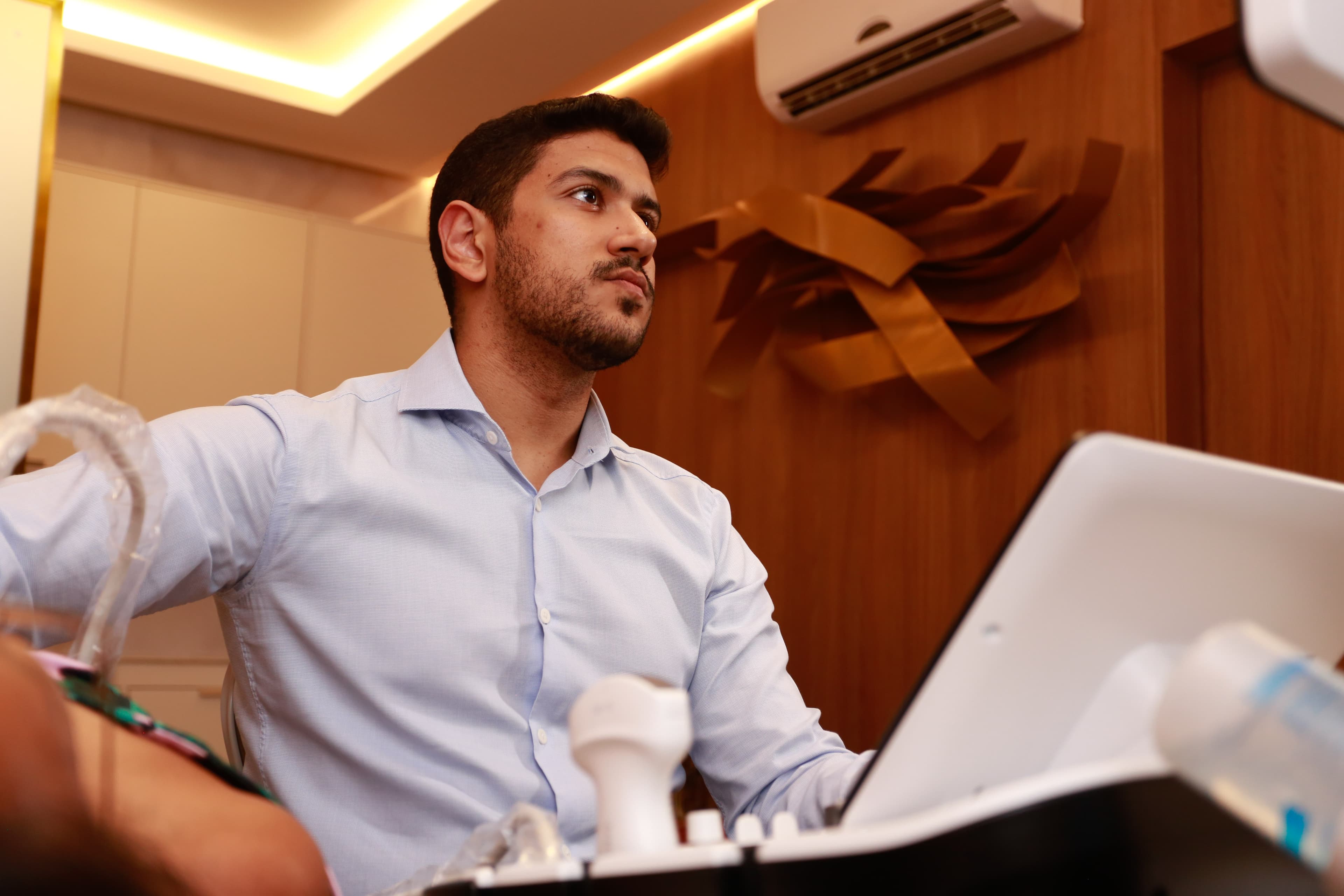 Male medical professional in a blue shirt performs an ultrasound scan in a clinical setting.